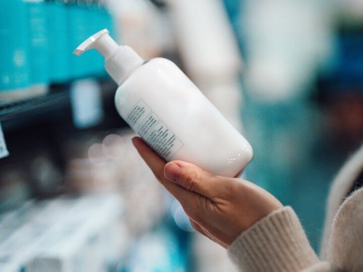 A consumer holds a packaging product in one hand  which is a pump action opaque white bottle that contains hand soap